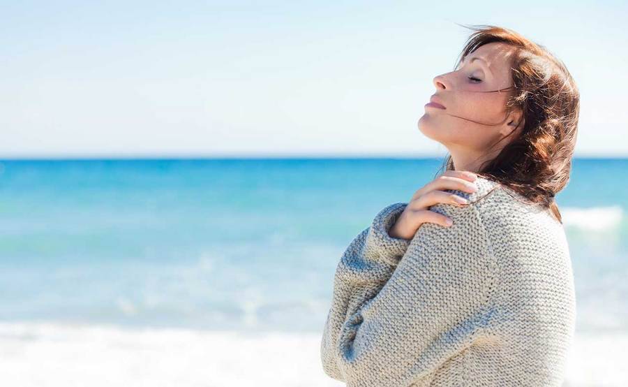 A calm middle-aged woman at the beach represents the full life that can be led after urethral cancer treatment.