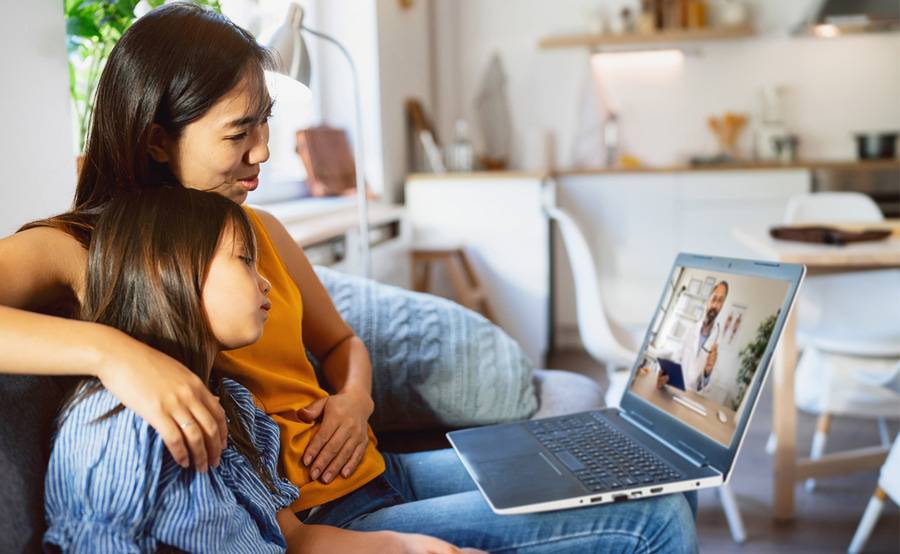 A mom in an orange shirt on a telemedicine call with her daughter.