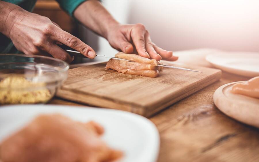 A cook prepares chicken meat on a board separate from other ingredients to prevent potential food poisoning.