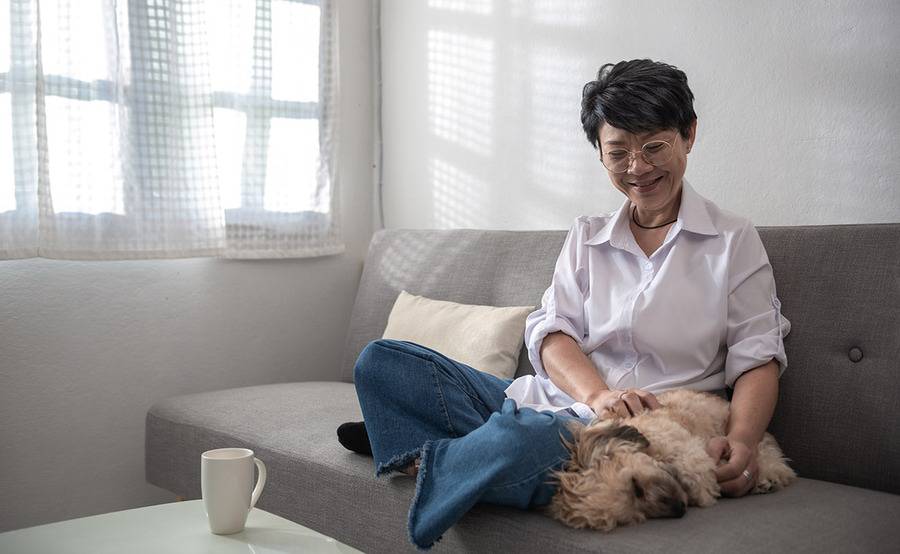 A woman sitting on her couch, smiling at her dog.