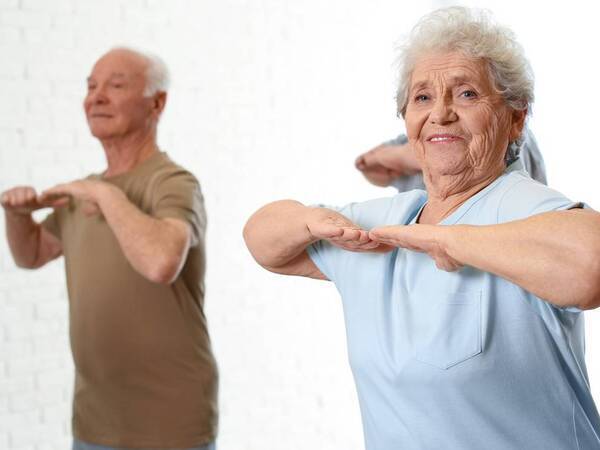 Three older adults, both men and women, participate in a group exercise to help with balance.