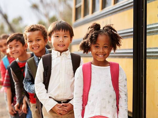 Group of young kids get ready to board a school bus for first day of new school year.