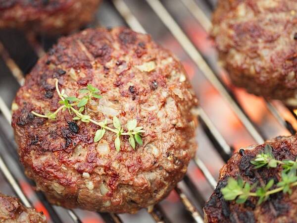 A hamburger patty on a grill with dressing. Is it good for you?