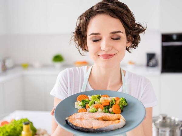 A young woman displays plate with fish and vegetables, a healthy meal.