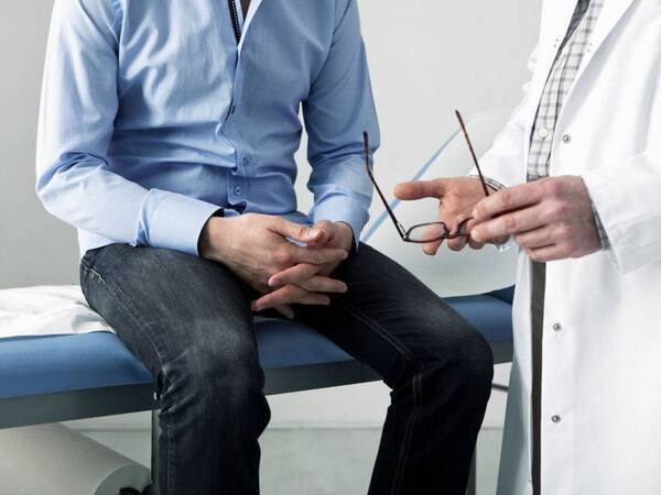 A man crosses his hands in a physical exam room discussing prostate cancer symptoms that he has experienced.