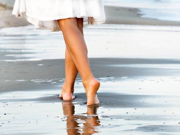 A woman walks on the beach is featured in a photo for a story about varicose vein prevention and treatment.