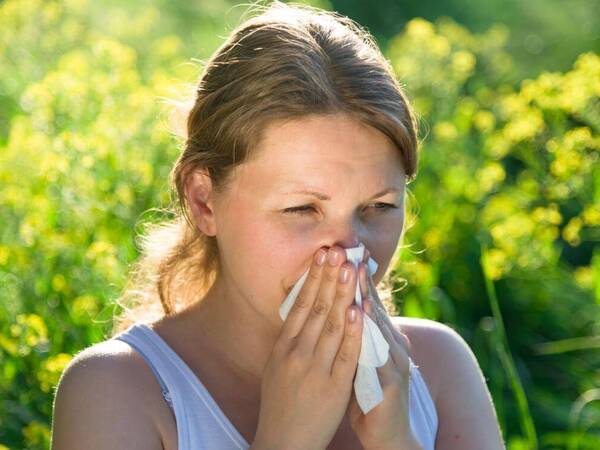 A woman wipes her nose after sneezing caused by allergies. 