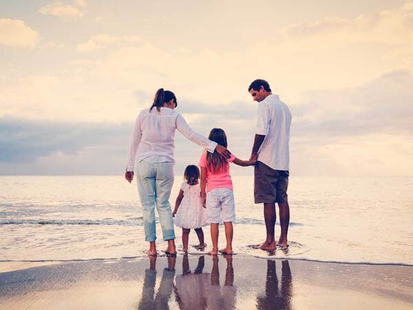Man, woman and two small children stand on the ocean shoreline on a cloudy day. 