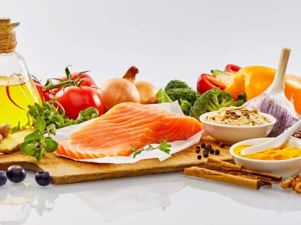 Foods that are commonly used for Mediterranean diet meals are displayed for an article on anti-inflammatory foods. A sample of Mediterranean Diet foods including salmon, broccoli, tomatoes, onions, blueberries, olive oil and walnuts.
