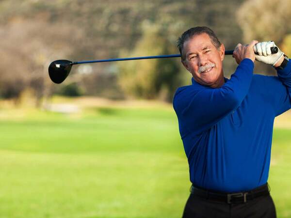 Scripps patient Garry Collins stands on a golf course swinging a golf club. 