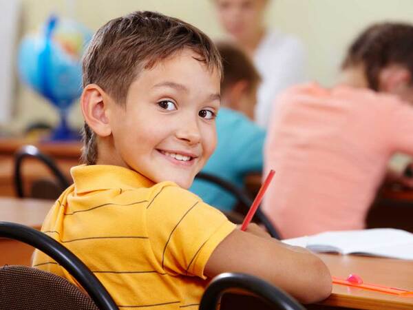 A smiling student diagnosed with ADHD turns around in his chair while working on an assignment in a classroom setting. 