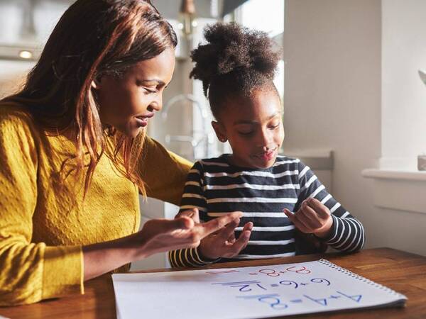 An African American mom helps her young daughter with her homework.