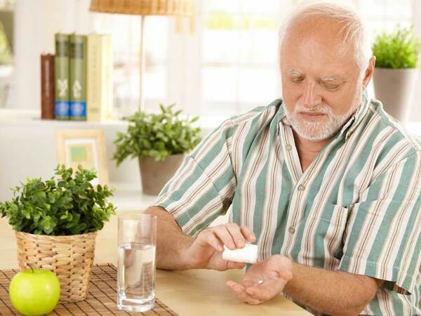 A man sitting at a table preparing to take a pill.
