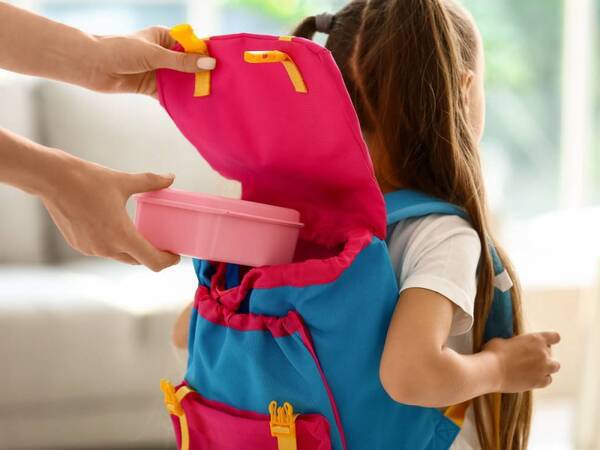 A young girl gets ready for school with a healthy lunch in her backpack.