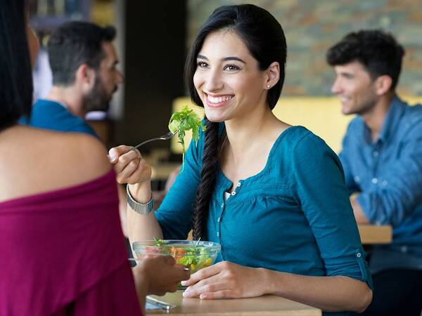 Two women enjoy healthy green salads together in a restaurant.