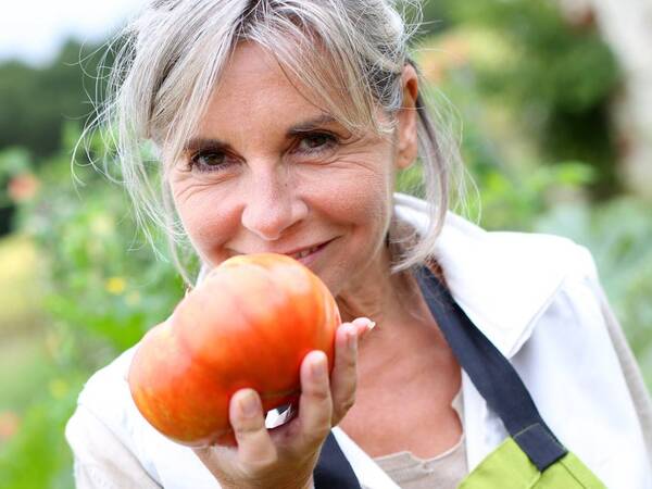 A woman enjoying spring time holding a ripe tomato ready to eat.
