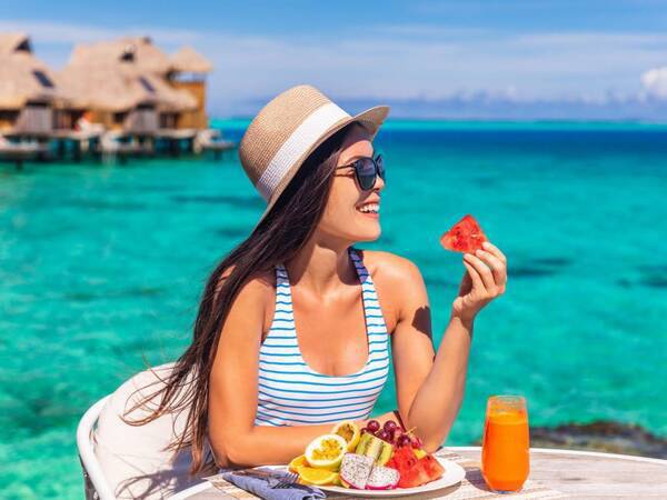 A young woman eats healthy during her vacation, water in the background.