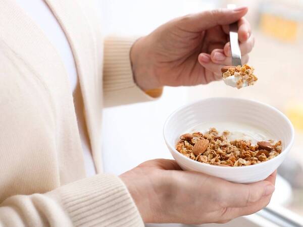 An older woman scoops protein-rich yogurt mixed with fiber-rich nuts.