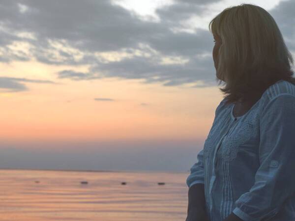 A woman contemplates menopause during sunset at the beach.