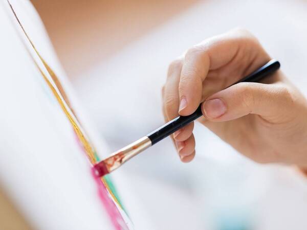 A hand holding a paint brush is seen in this photo that is being used to illustrate a post on the healing arts program at Scripps Encinitas for patients recovering from brain injuries.