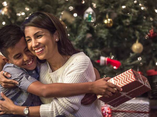 A young mother hugs her son with a Christmas tree in the background.