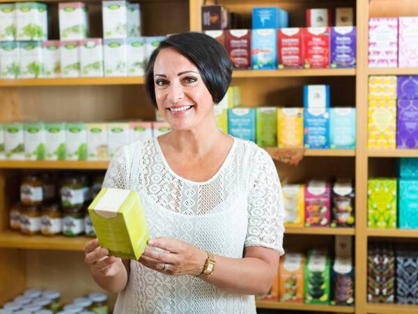 A mature woman at a natural supplements store holds a box with dietary supplements.