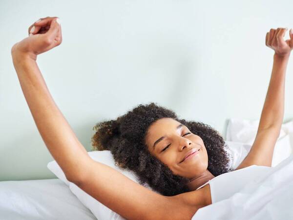A woman smiles and stretches as she awakens in bed, feeling refreshed and alert after a good night’s sleep.