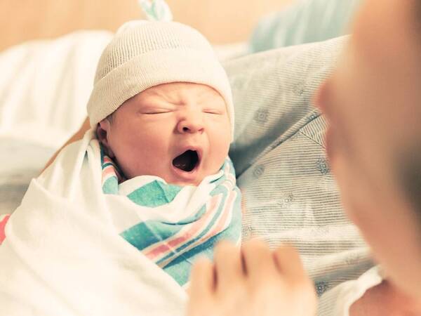 A newborn baby in hospital maternity ward yawns.