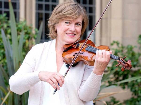 A woman holding a violin and smiling for a photo