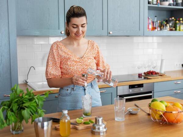 A woman in her kitchen creates a healthier non-alcoholic beverage with sparkling water, lime and oranges. 