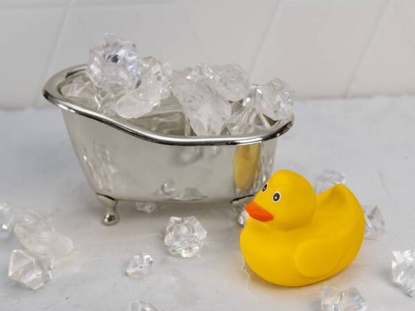 An image of ice and a rubber duckie in a bathtub illustrates article on the risks and benefits of ice baths.