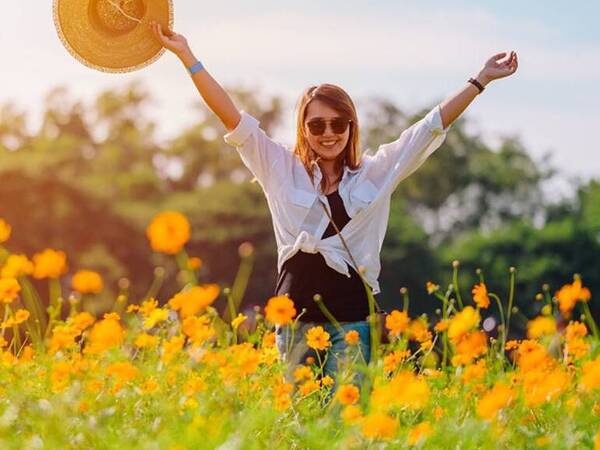 A young woman rejoices in a field of yellow flowers.
