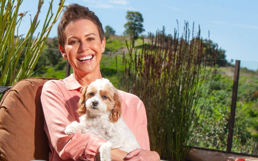 Kelly O'Connor smiles at home outdoors holding her small dog after breast cancer treatment.