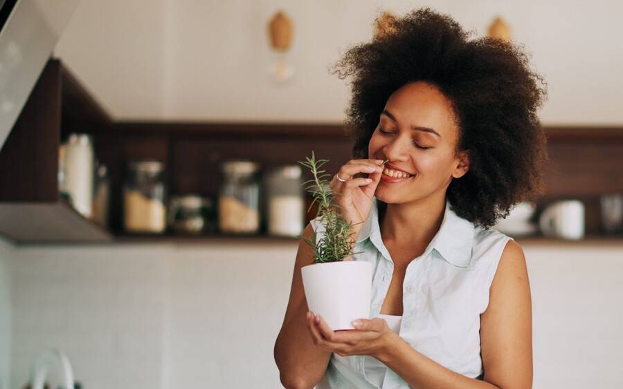 A young woman smells fresh healthy herbs she grew at home.