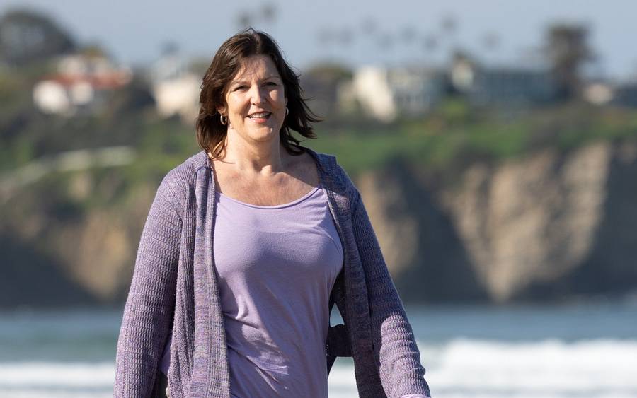 A mature woman in lavender clothing, walks along La Jolla shores and is happy about her breast cancer care at Scripps.