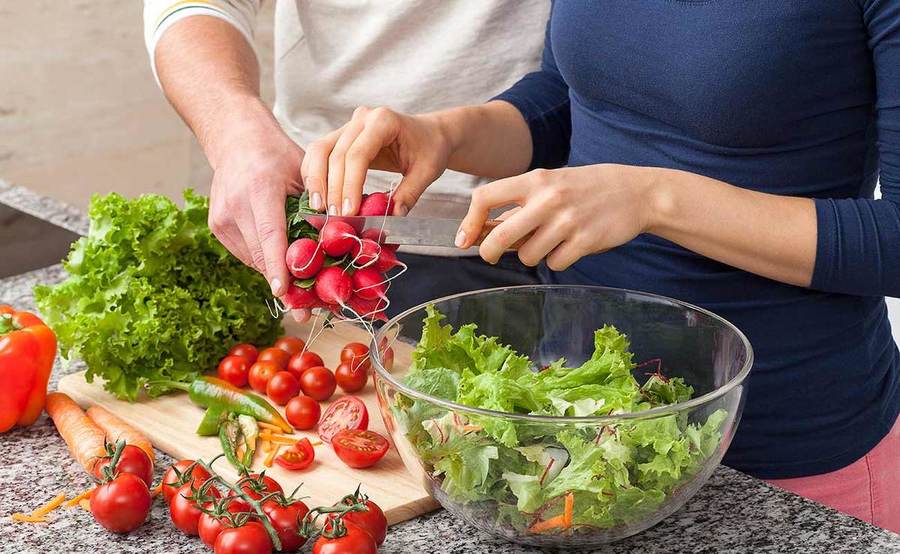 Two people's hands make a fresh salad with radishes and tomatoes, representing personalized diabetes management.