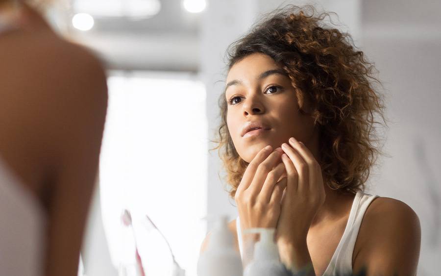 A young woman looks at a pimple in her mirror.