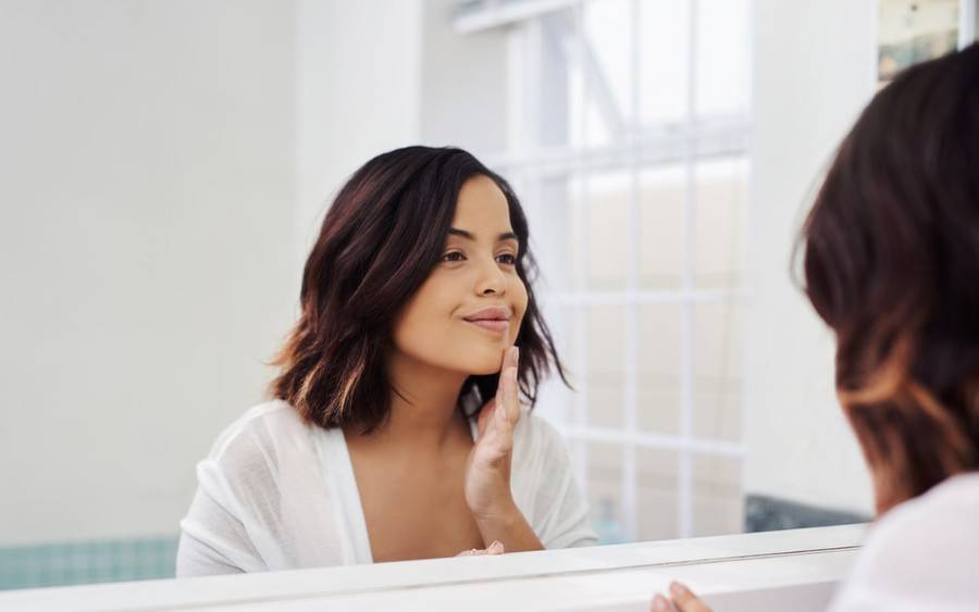 Woman smiles looking at her acne scarless face in mirror.