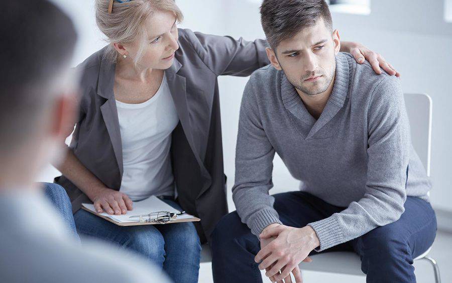 A counselor puts her arm around a young man, representing the comfort and compassion that can be found in a grief support group after an overdose.