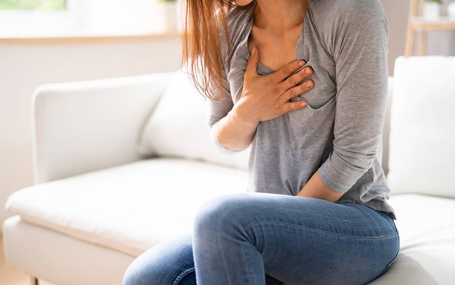 A woman grabs her chest, experiencing symptoms of atrial fibrillation, AFib.