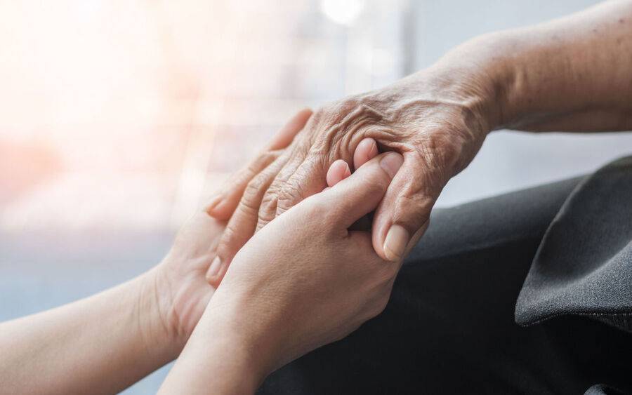 A caregiver holds the hand of an elderly Alzheimer's Disease patient.
