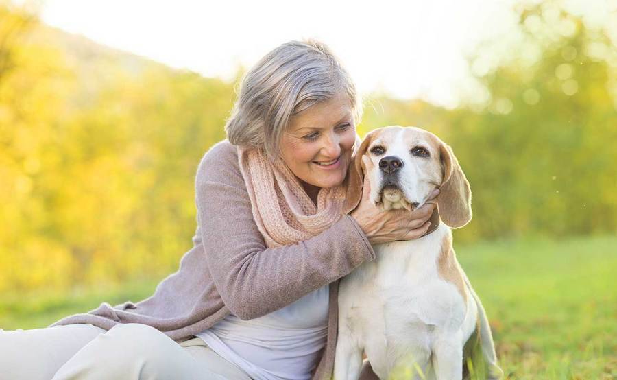 A smiling mature woman plays with her dog outdoors, representing the full life that can be led after anal cancer treatment.
