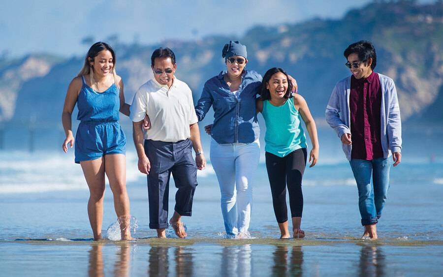 Angela Flores, a Scripps MD Anderson cancer patient, happily walks along the beach with her family after beating cancer.