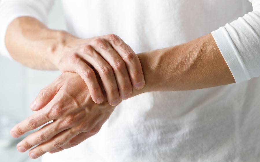 An older woman grabs her wrist. She's in pain due to arthritis.