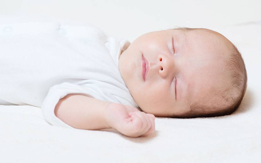 A newborn baby peacefully sleeps on its back.