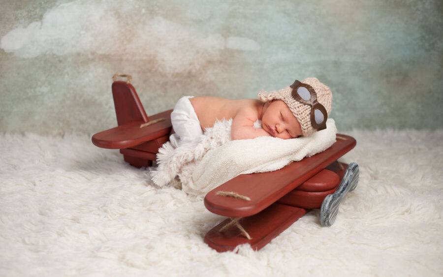 A baby sleeps in a blanket and airplane-shaped bed.