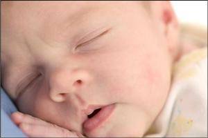 A baby sleeps on a caregiver's chest, representing one of the early parenting topics covered in the Childbirth Preparation course at Scripps Health.