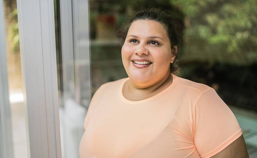 A woman wearing an orange shirt smiles as she considers bariatric surgery.