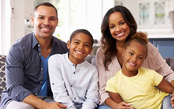 A family of four smiling and sitting together on teh couch.