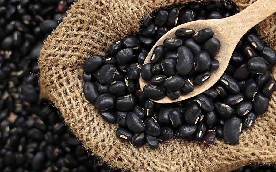 Dried black beans in a burlap bag with a wooden spoon represent the types of superfoods you can plant in your garden.